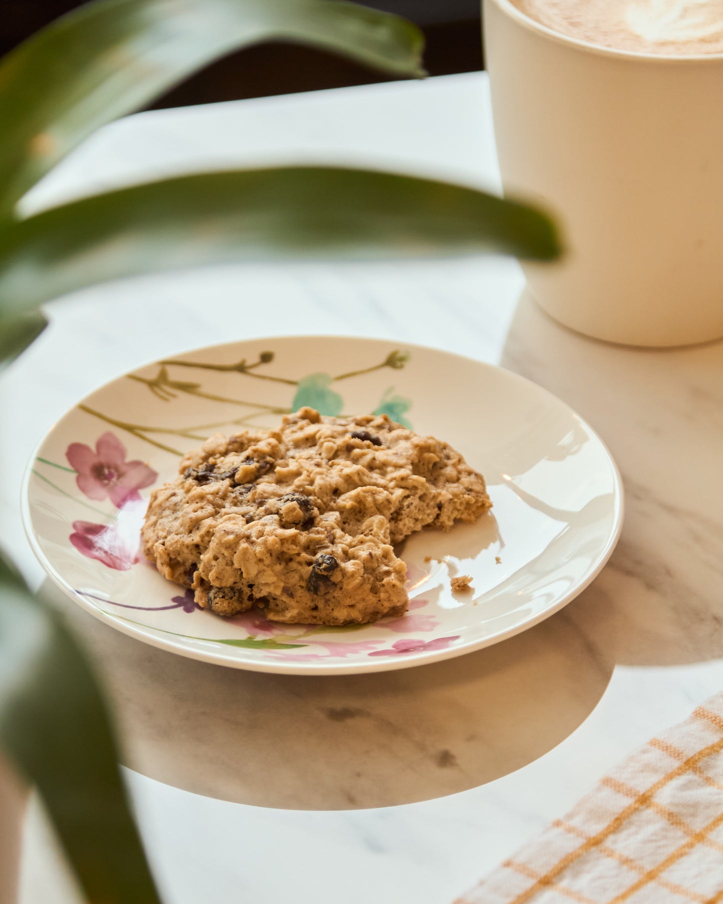 Two nutritious clean-label cookies with oats and raisins on floral plate, next to coffee mug, family-friendly Canadian.